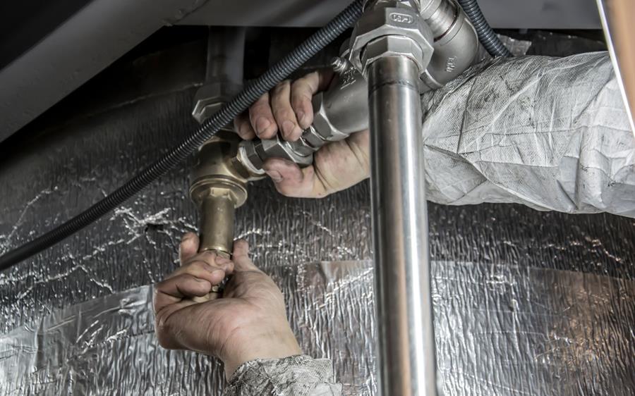 Mainile unui instalator monteaza fitinguri metalice pe traseul de apa